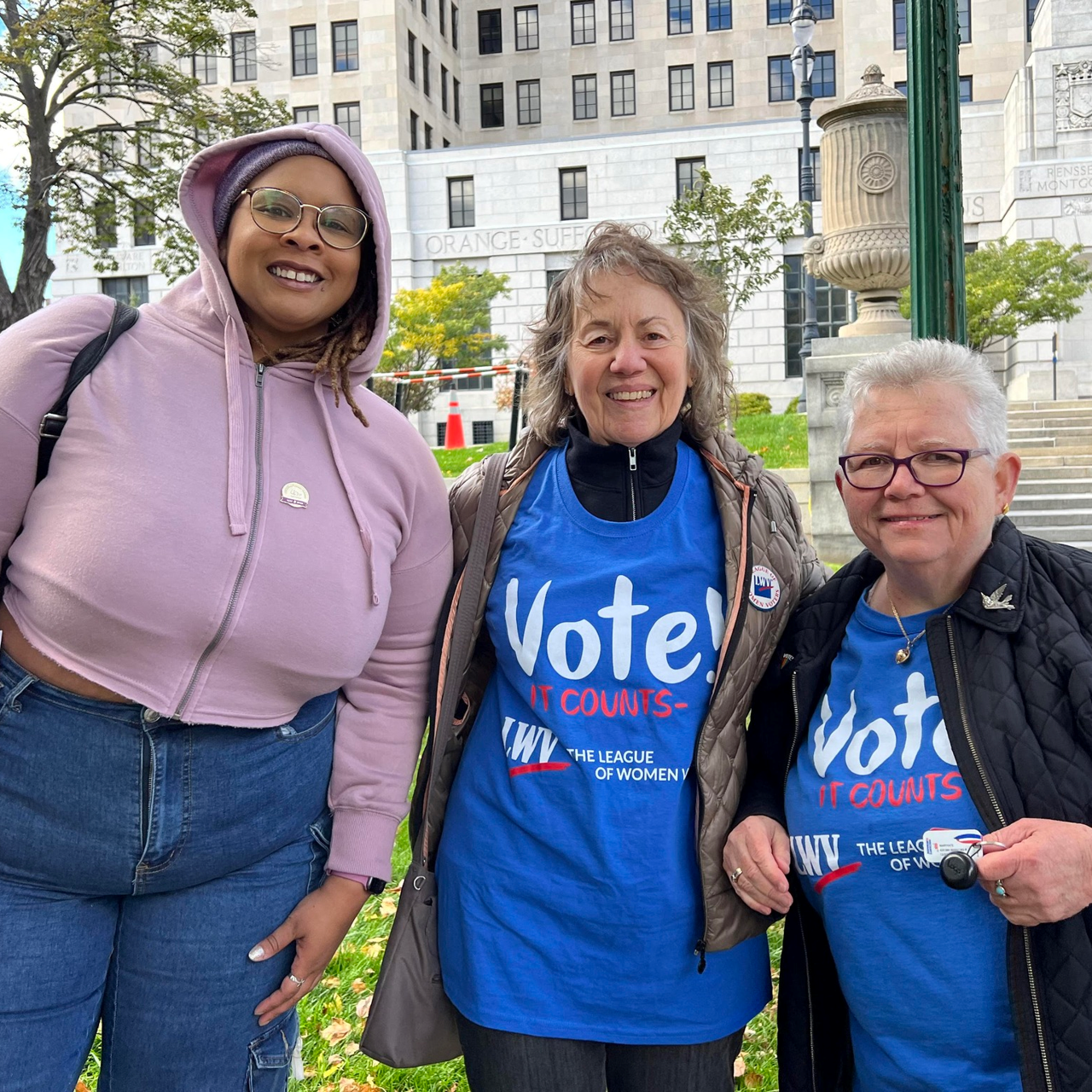 Three women in blue t - shirts standing in front of a building.