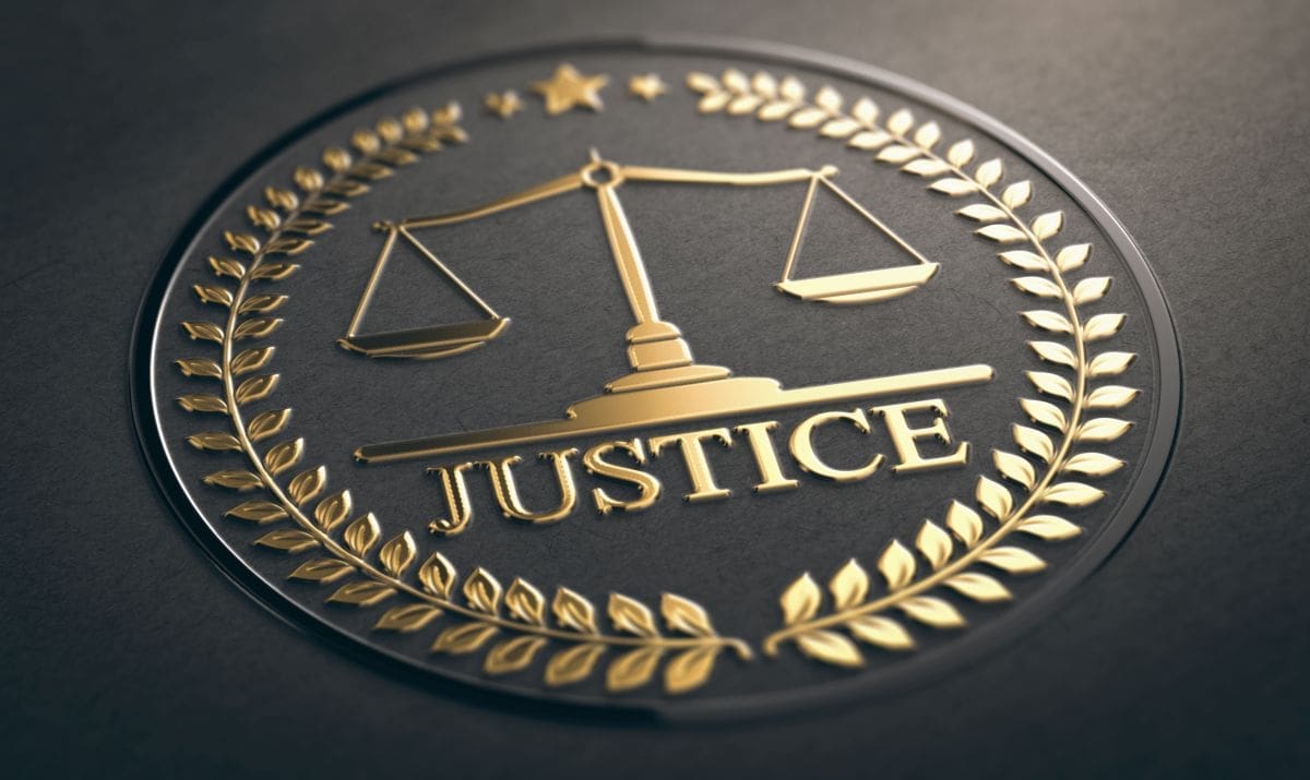 A gold emblem featuring balanced scales, laurel wreaths, a star, and the word "JUSTICE" on a dark background.